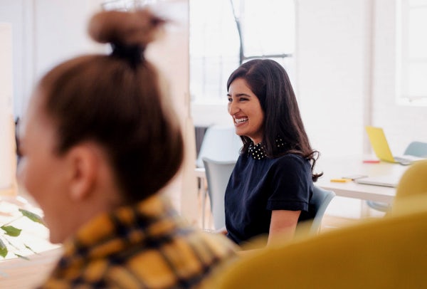 Smiling woman, wearing a blue shirt with an out of focus person in the foreground
